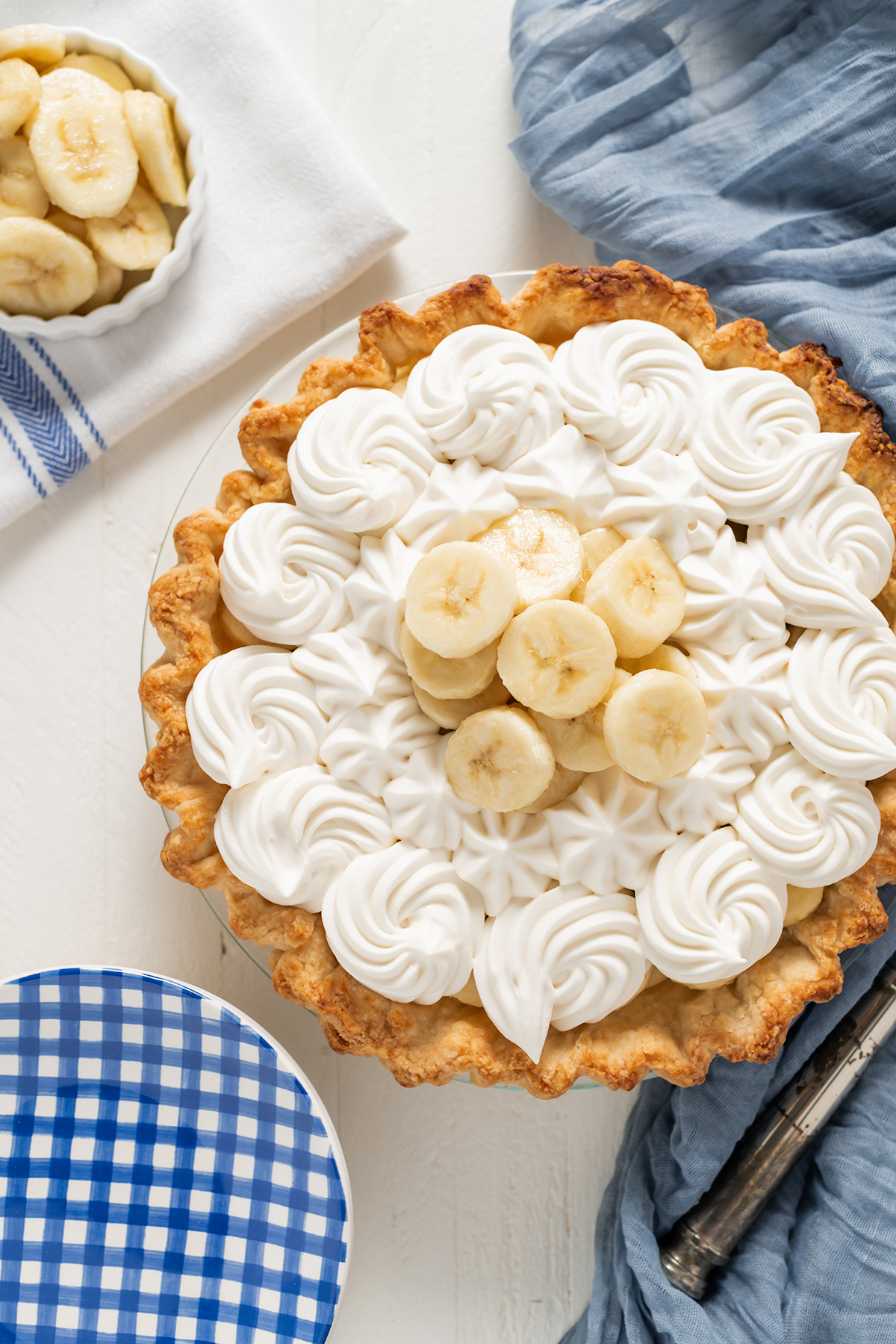 Overhead shot of Banana Cream Pie with blue gingham plates and blue towel.