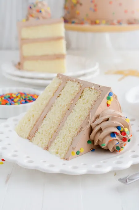 Yellow Birthday Cake with Chocolate Buttercream cake slice on its side on plate.