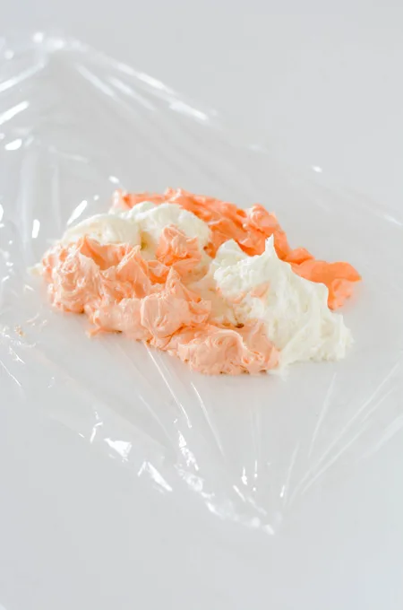 Orange Creamsicle Layer Cake colored frosting on plastic wrap.