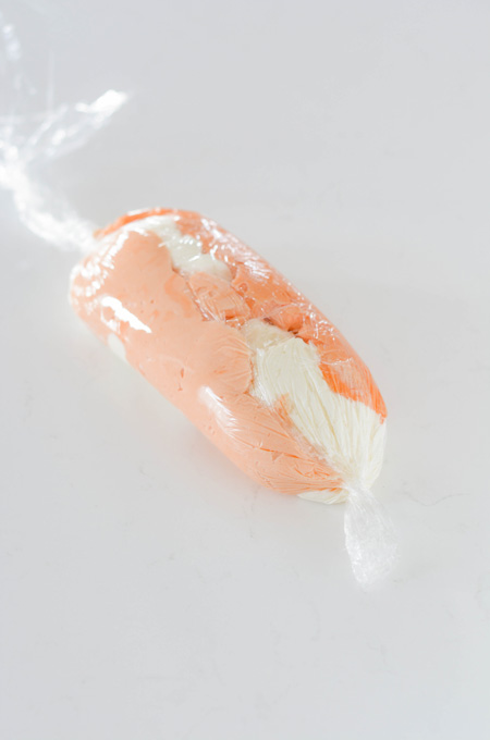 Orange Creamsicle Layer Cake colored frosting wrapped up in plastic wrap.
