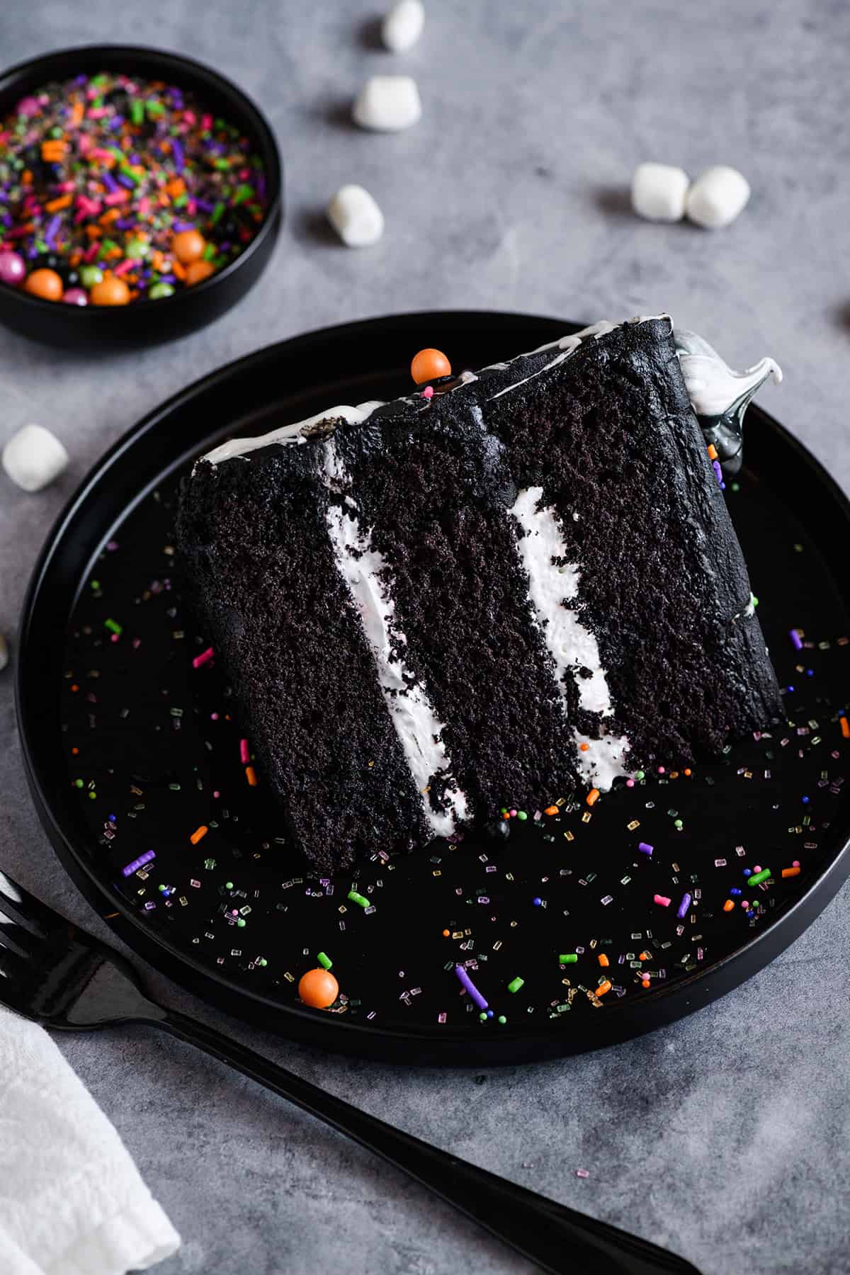 Three quarter angle of sliced Black Velvet Halloween Cake on black plate with sprinkles.