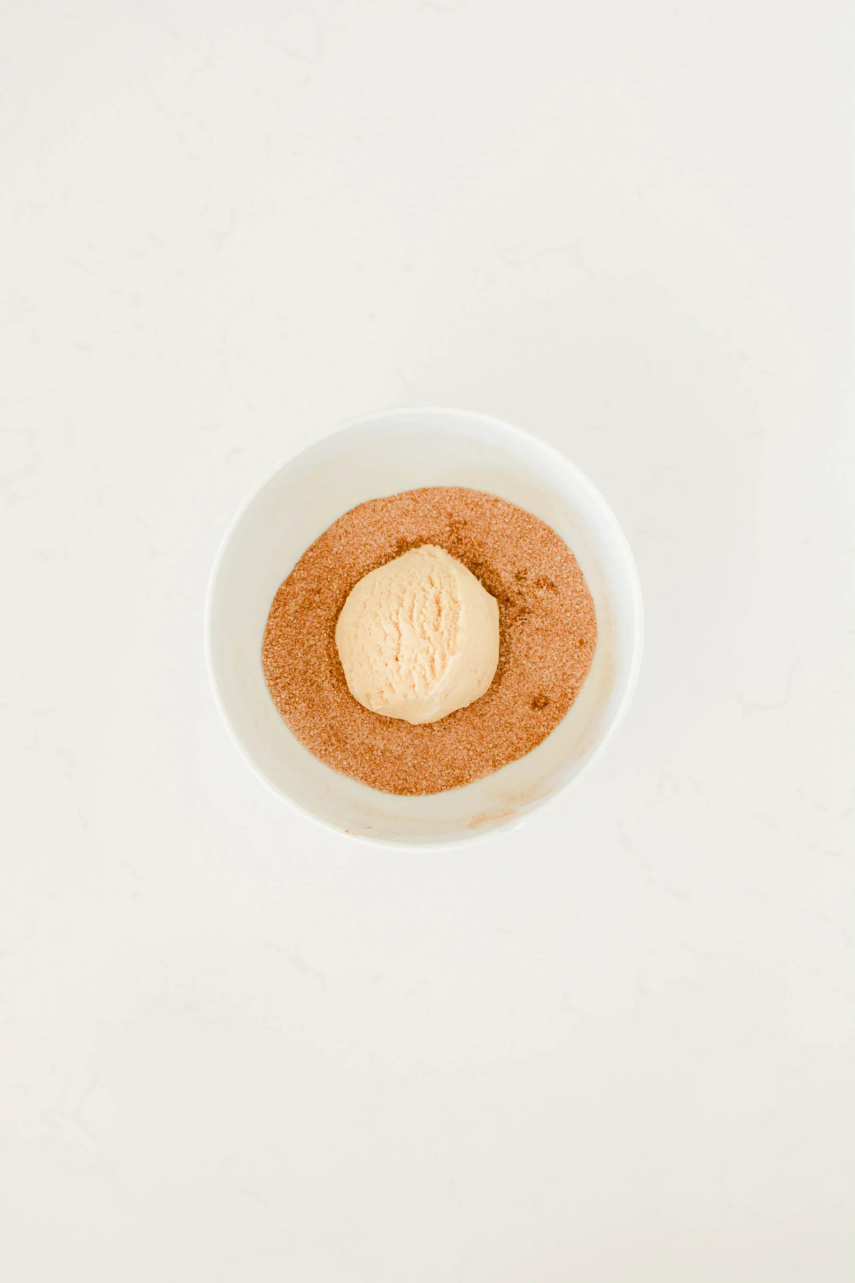 Overhead shot of cookie dough ball in cinnamon-sugar mixture for Snickerdoodles.