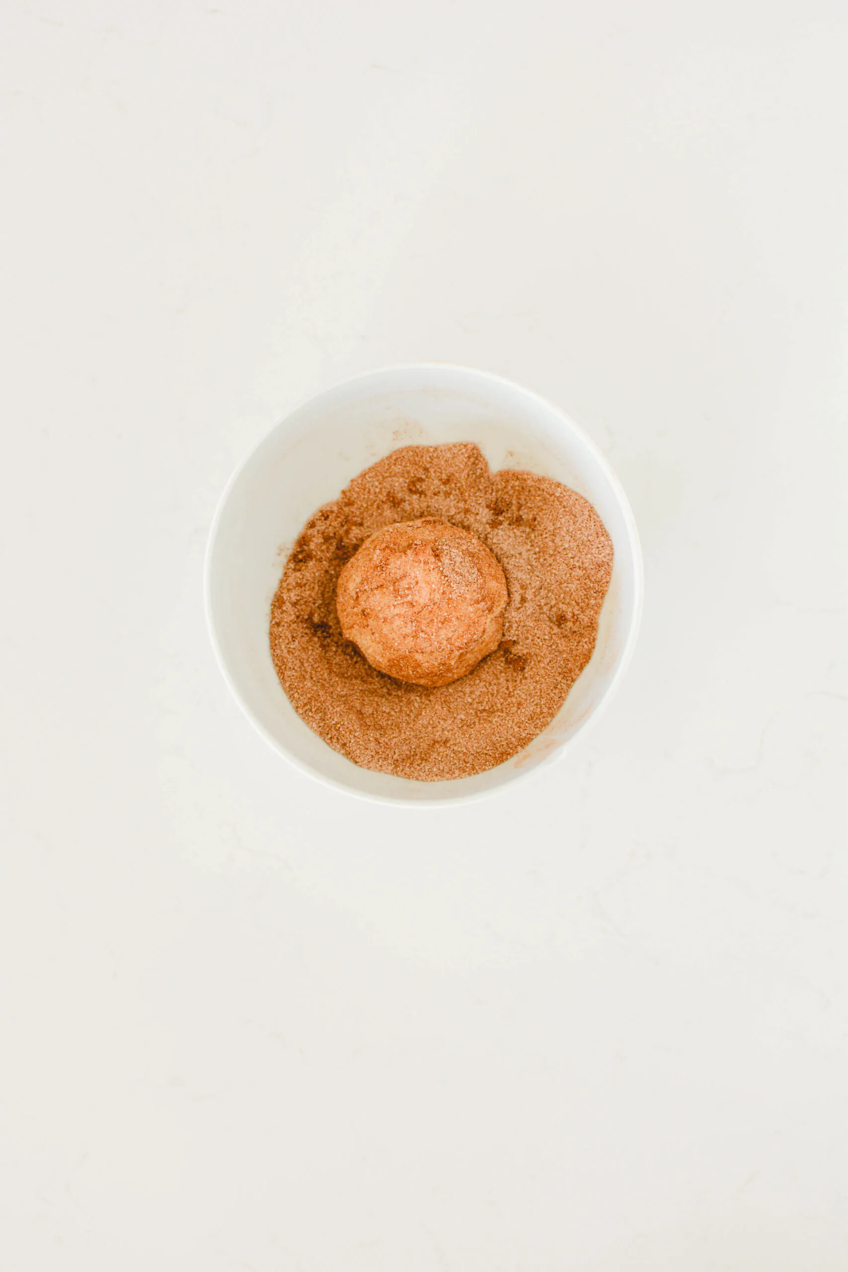 Overhead shot of cookie dough ball covered in cinnamon-sugar mixture for Snickerdoodles.