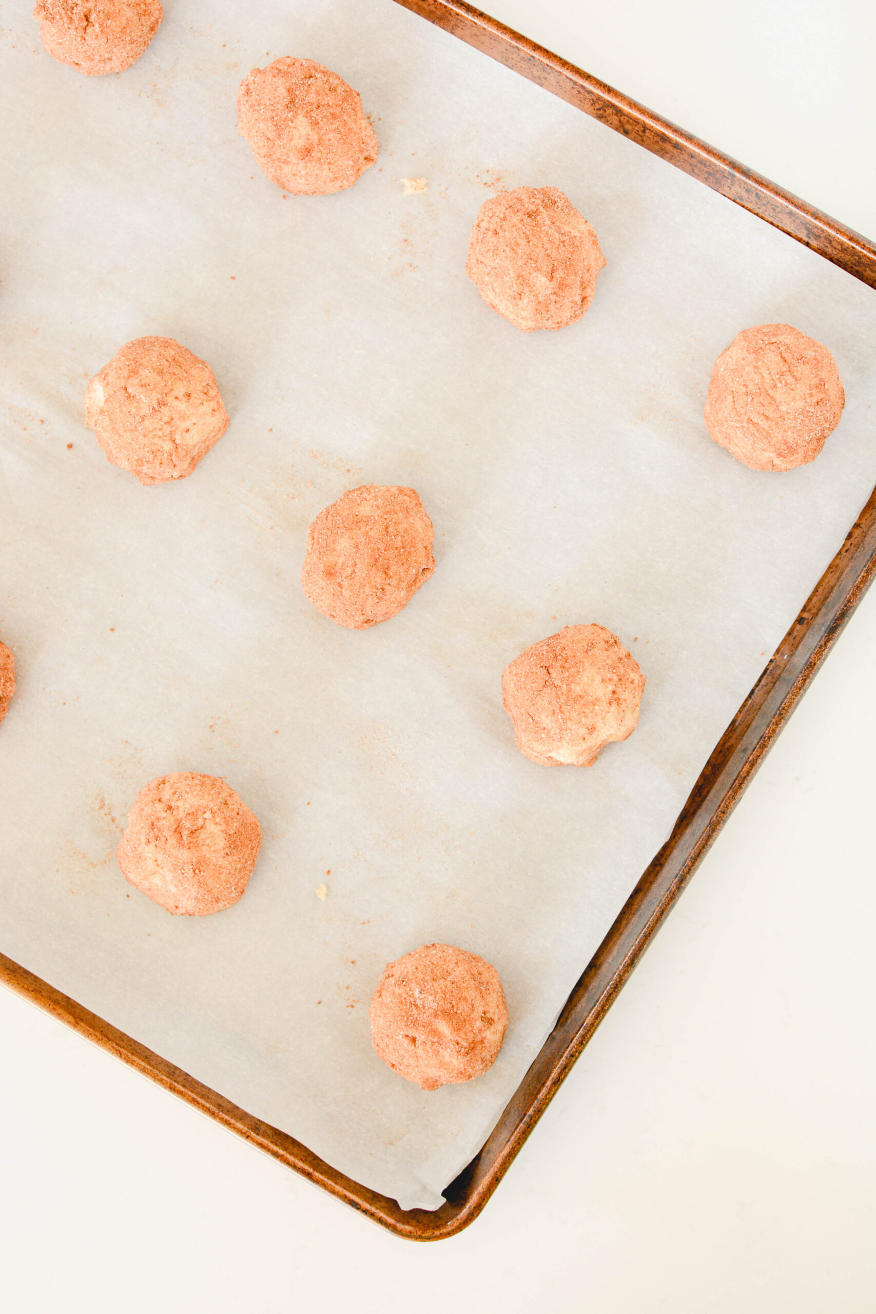 Overhead shot of cookie dough balls on lined baking sheet for Snickerdoodles.