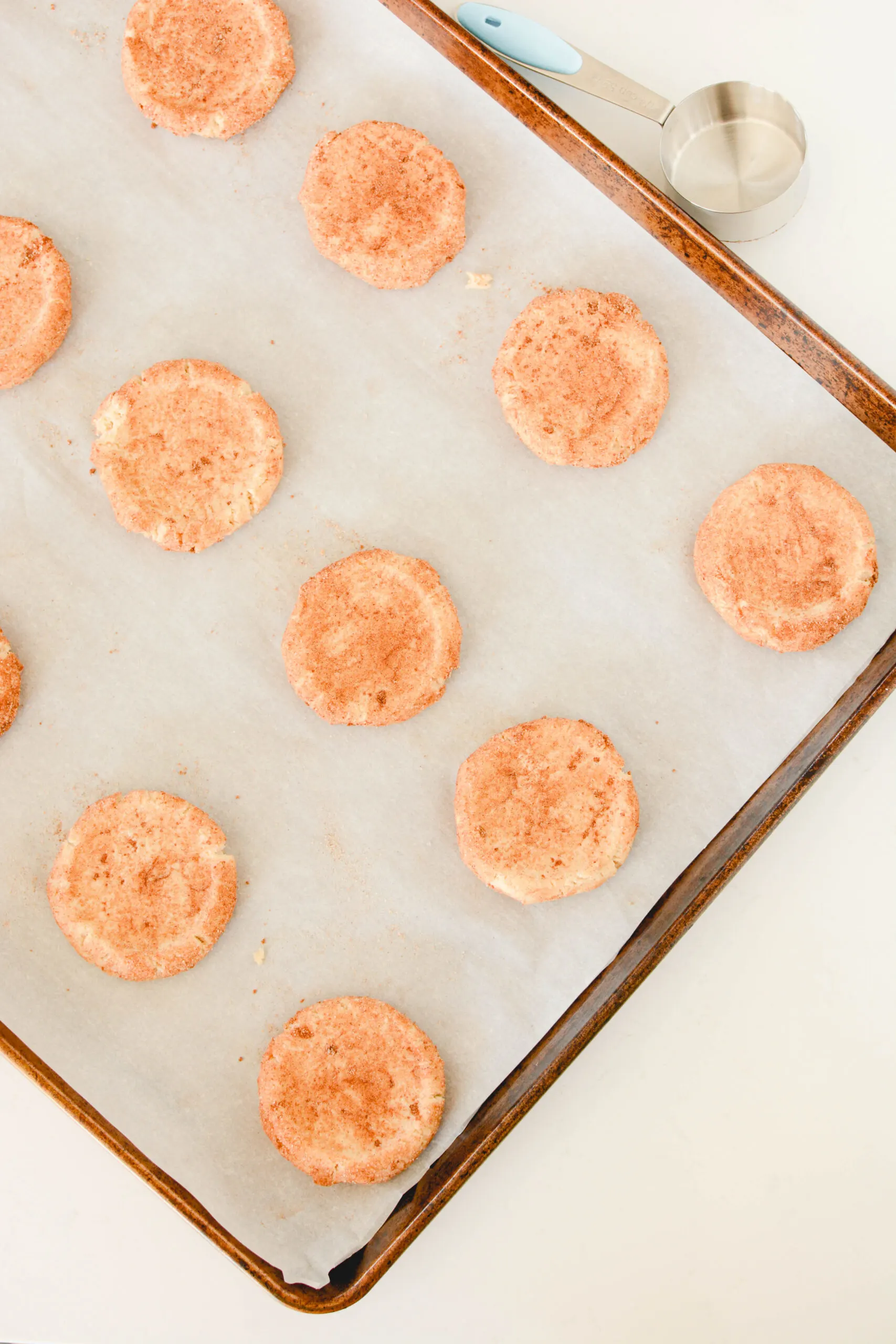 Overhead shot of flattened cookie dough balls on lined baking sheet for Snickerdoodles.