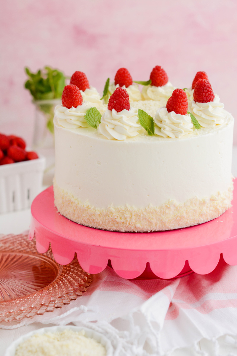Close up at three quarter angle of White Chocolate Raspberry Cake on pink cake pedestal.