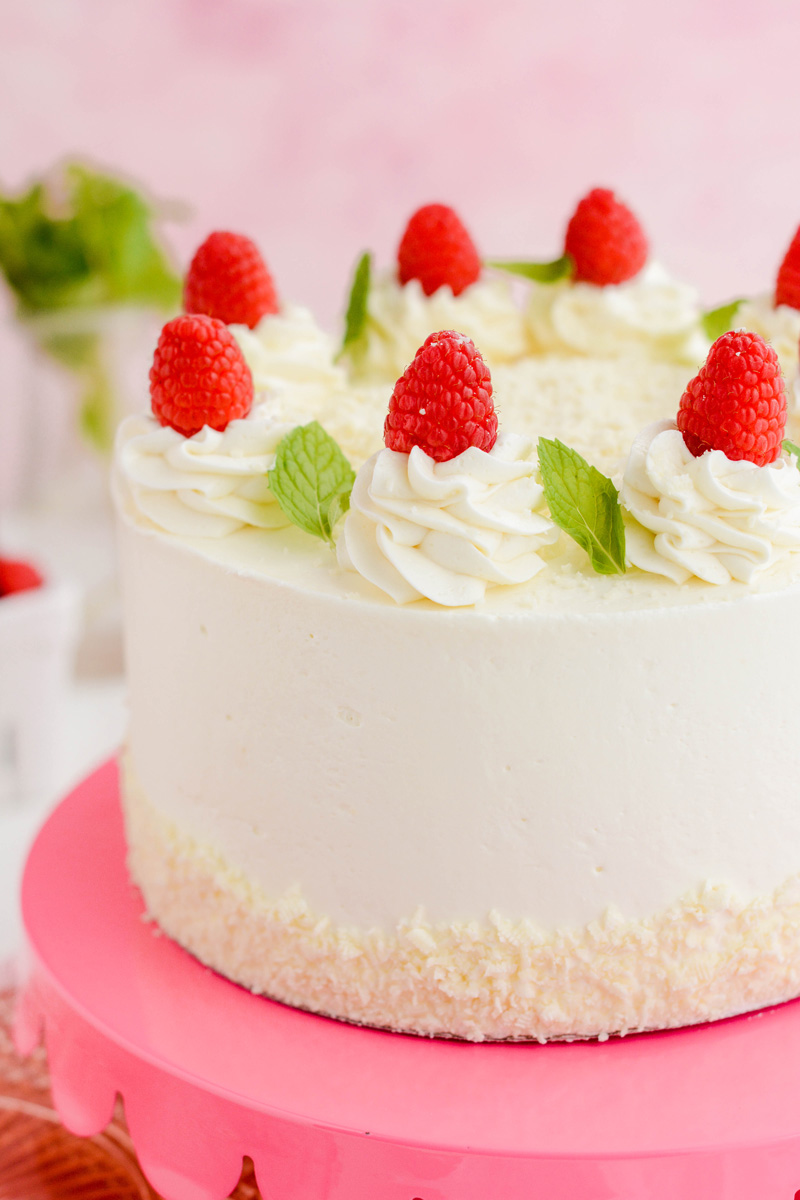Close up of cake fresh raspberries, mint and frosting swirls on White Chocolate Raspberry Cake.