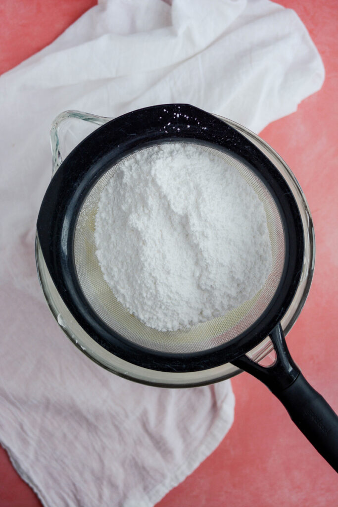 Overhead shot of powdered sugar in a sieve for White Chocolate Raspberry Cake.