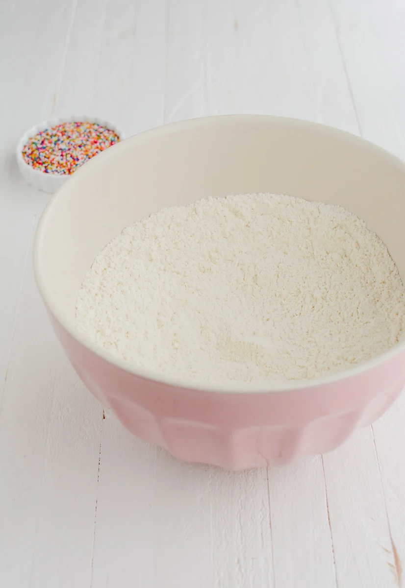 Three quarter angle of dry ingredients in antique pink mixing bowl for Mexican Sprinkle Cookies.
