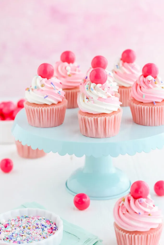 Three quarter angle Pink Bubble Gum Cupcakes on teal cake pedestal.