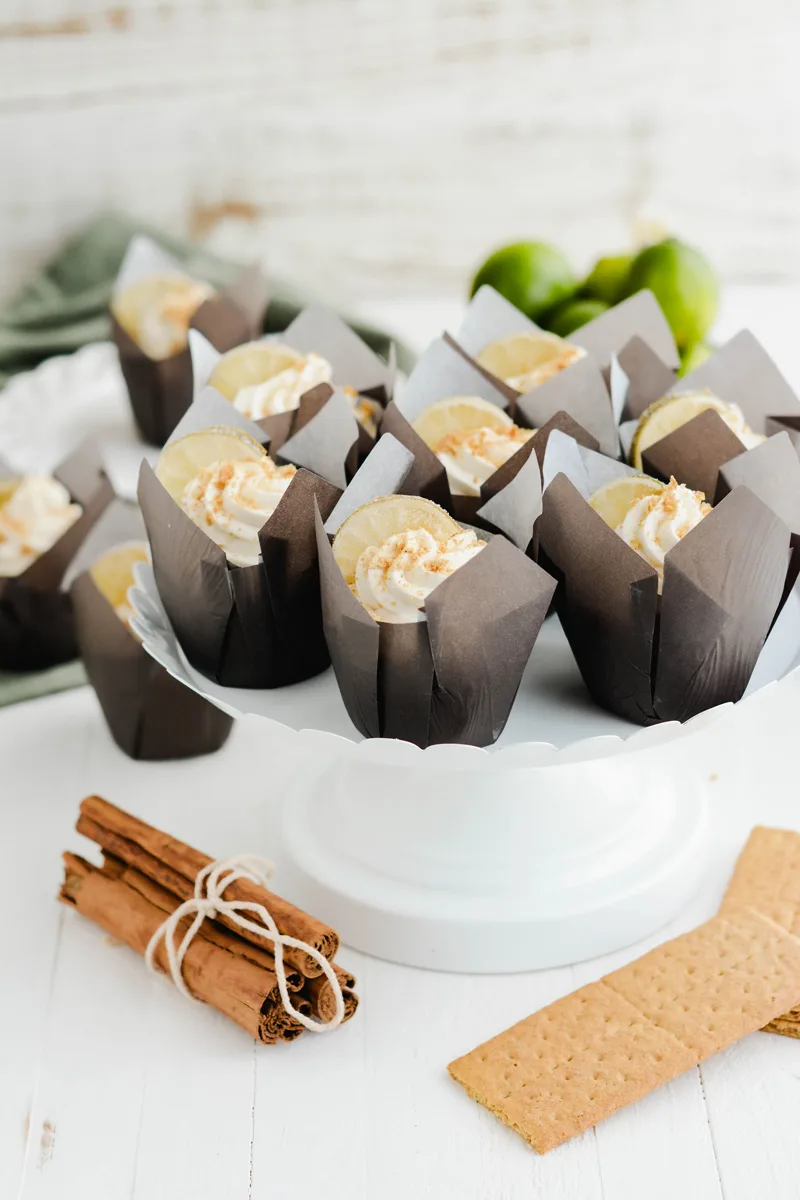 Key Lime Pie Cupcakes on white cake stand with cinnamon sticks.