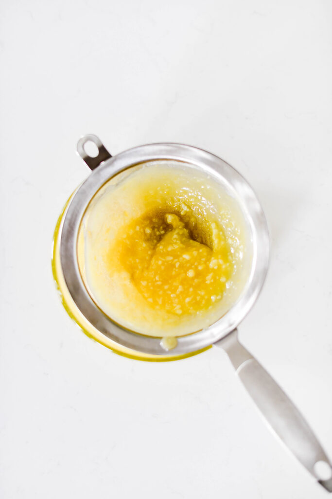 Strained lemon curd in sieve for Lavender Lemon Cupcakes.