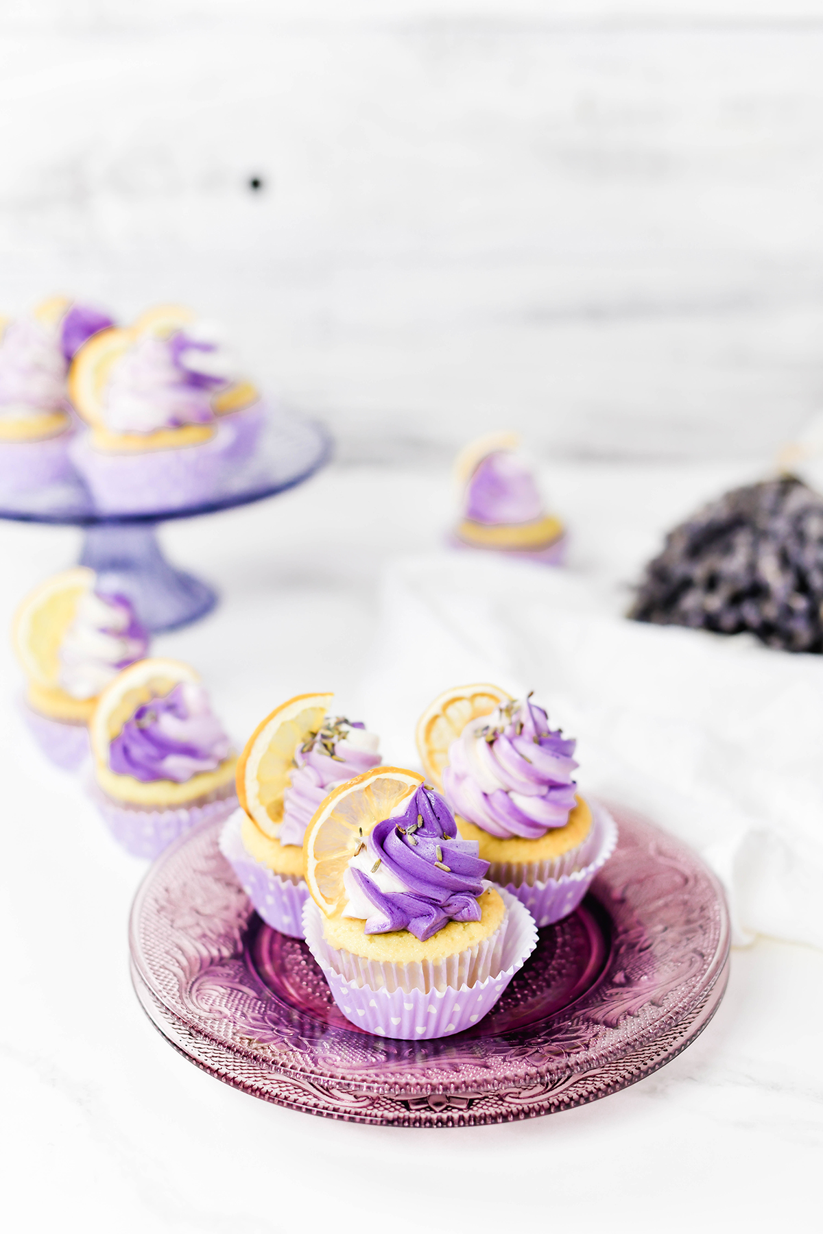 Wide open shot of Lavender Lemon Cupcakes on lavender cake plate and cake stand.