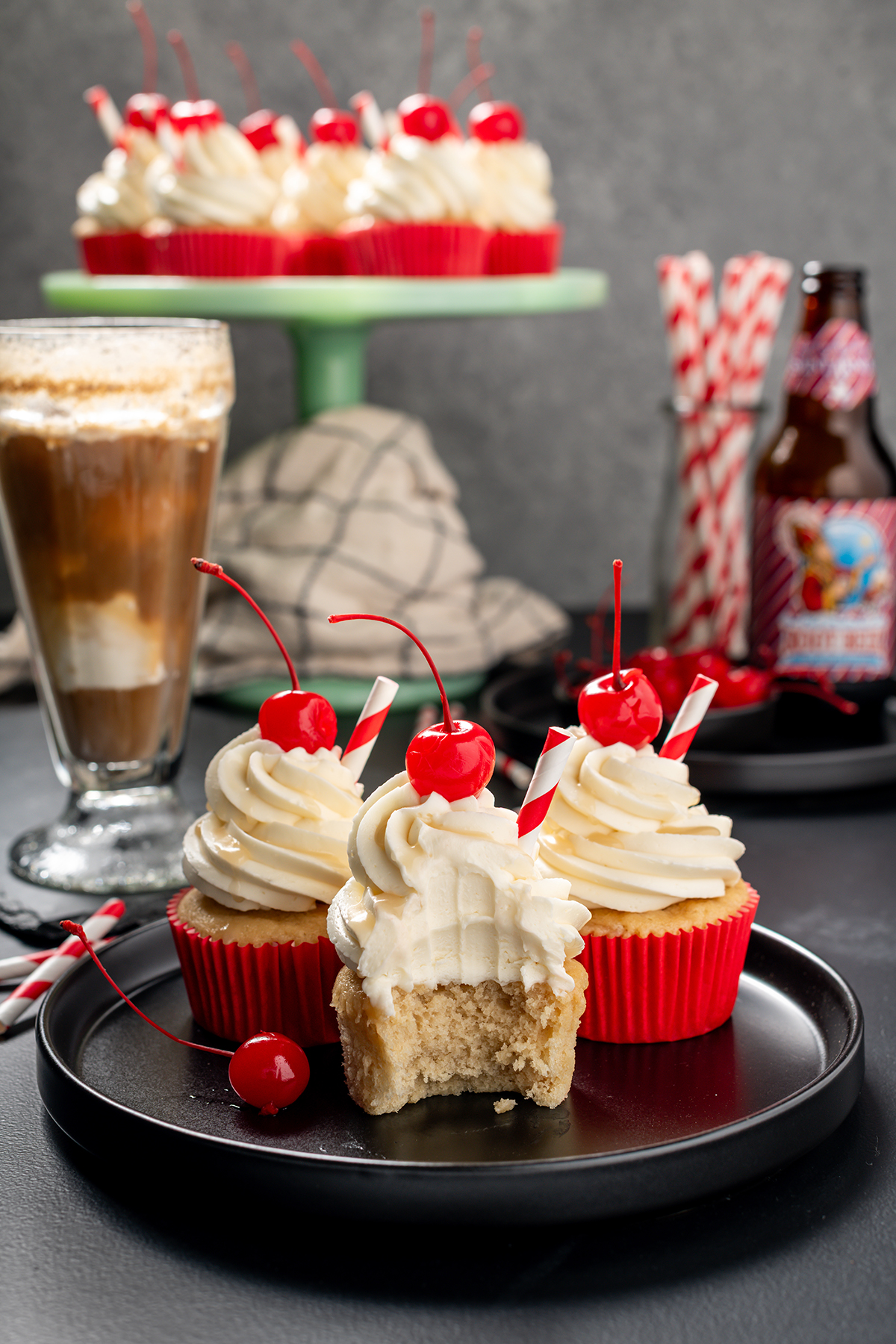 Shot of three Root Beer Float Cupcakes on black plate with a bite removed from one of the cupcakes.