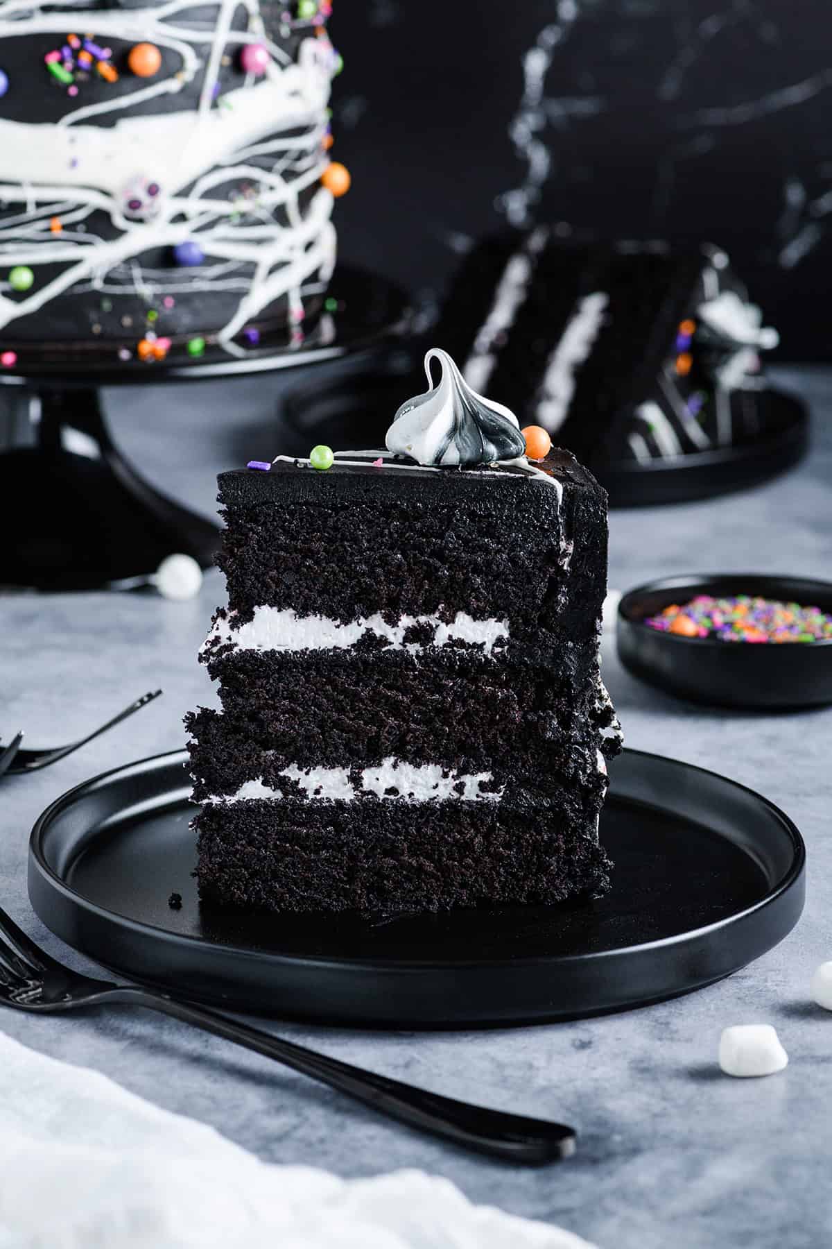 Straight on shot of sliced Black Velvet Halloween Cake sitting up with cake and sliced cake in the background.