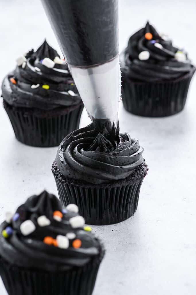 Three quarter angle of Black Velvet Halloween Cupcakes being frosted.