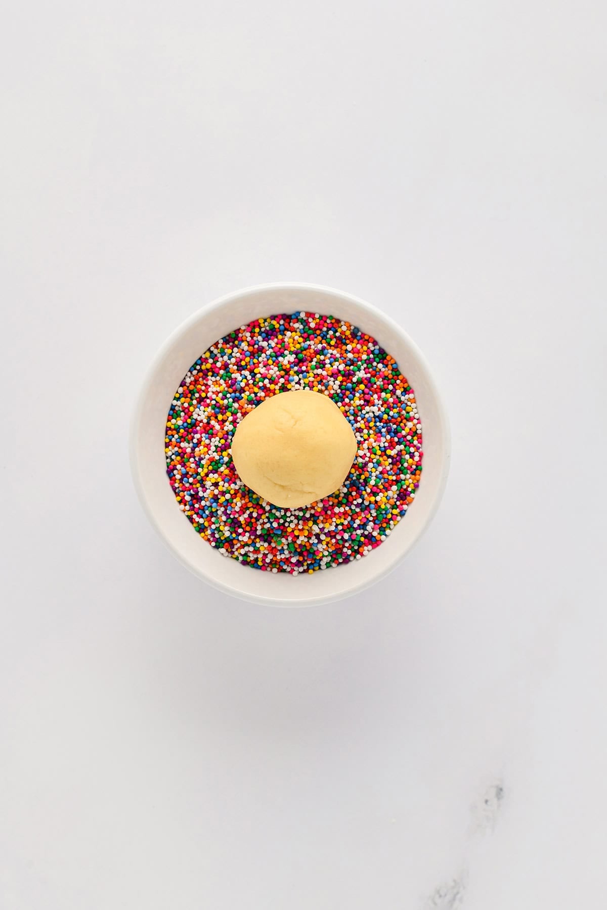 Overhead shot of dough ball in bowl of sprinkles for Mexican Sprinkle Cookies.