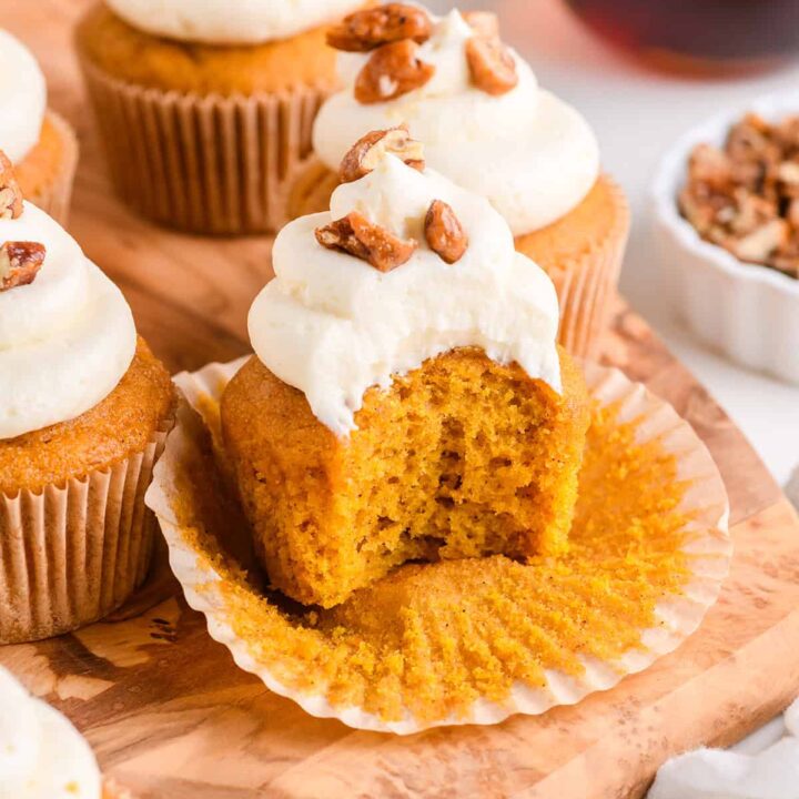 Close up shot of Pumpkin Cupcakes with Maple Cream Cheese Frosting with bite on wood serving board.