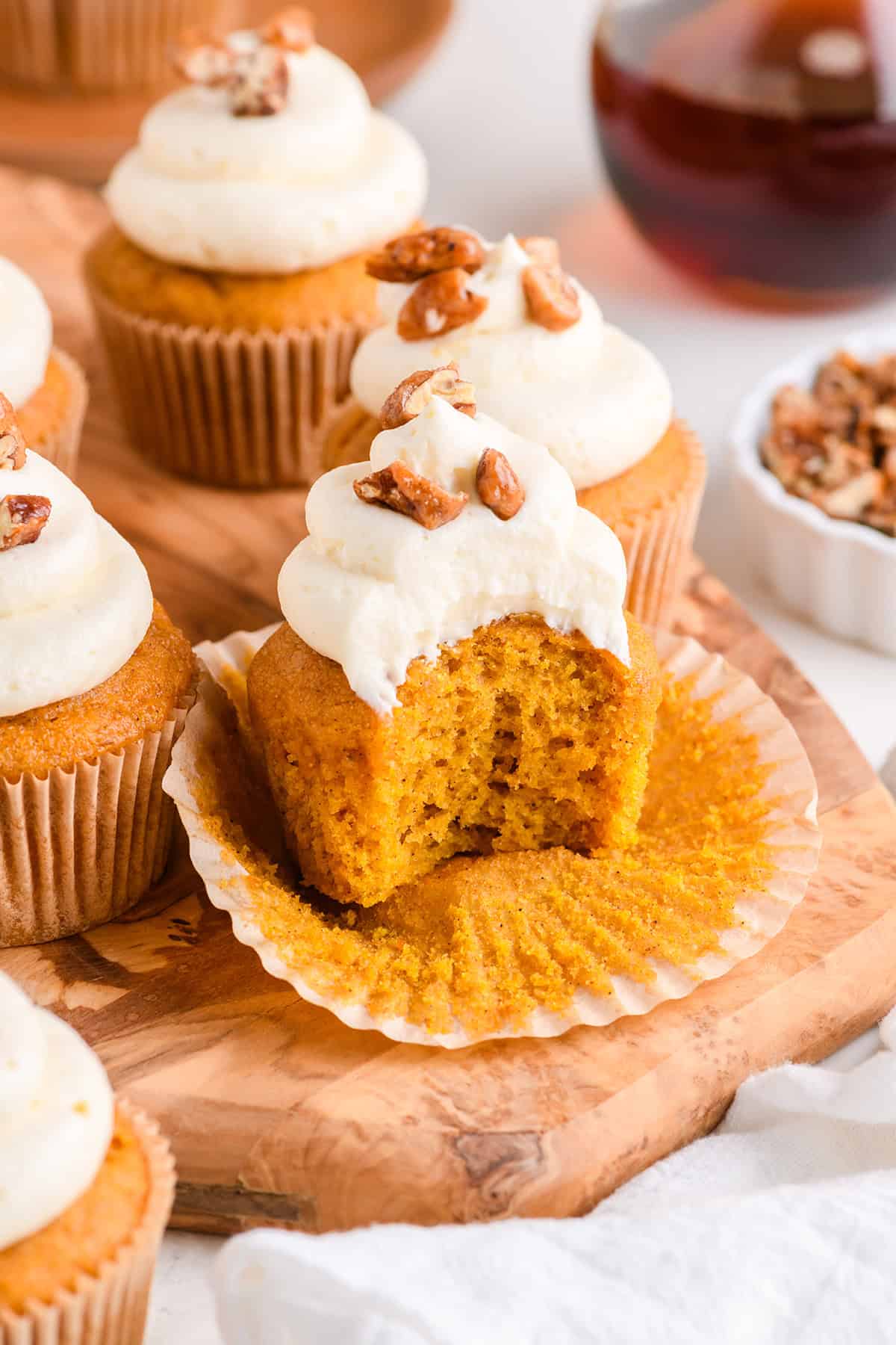 Close up shot of Pumpkin Cupcakes with Maple Cream Cheese Frosting with bite on wood serving board.