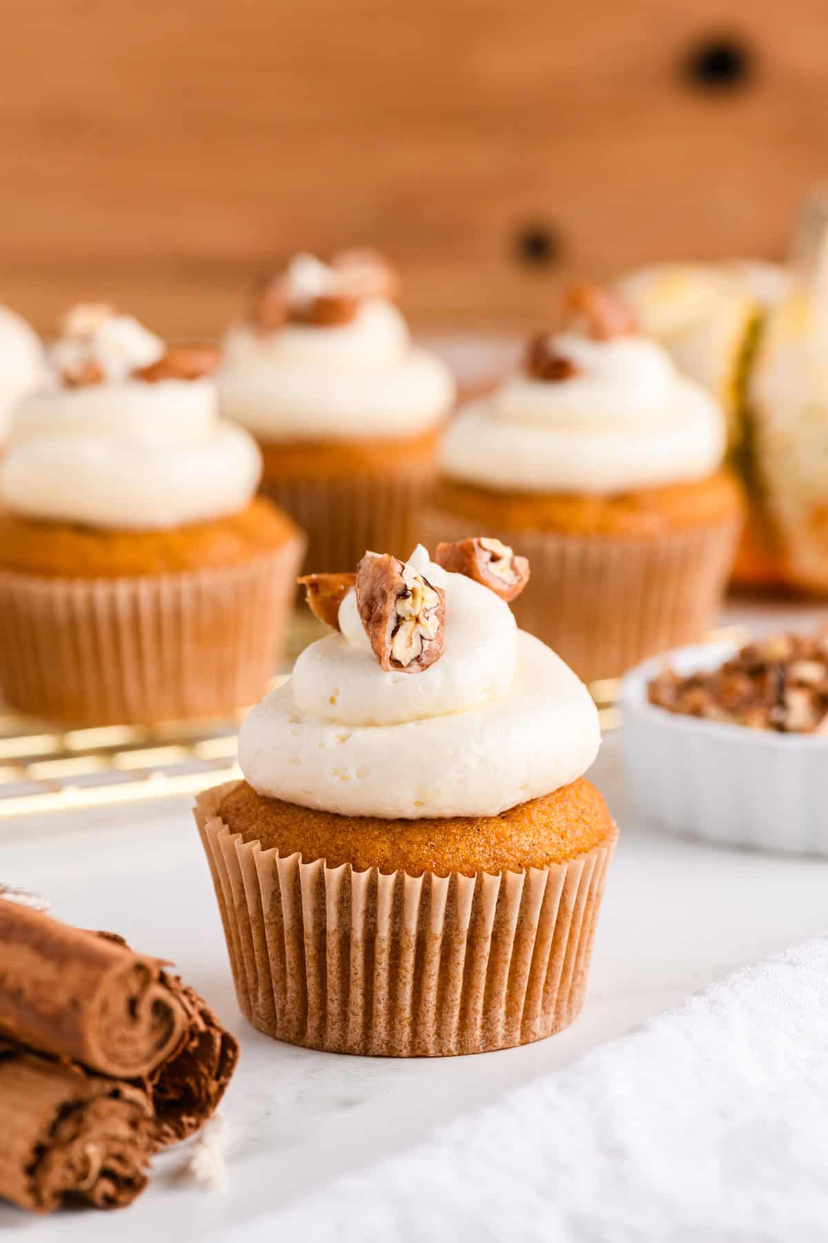 Single Pumpkin Cupcake with Maple Cream Cheese Frosting on white marble board with cupcakes in the background on cooling rack.