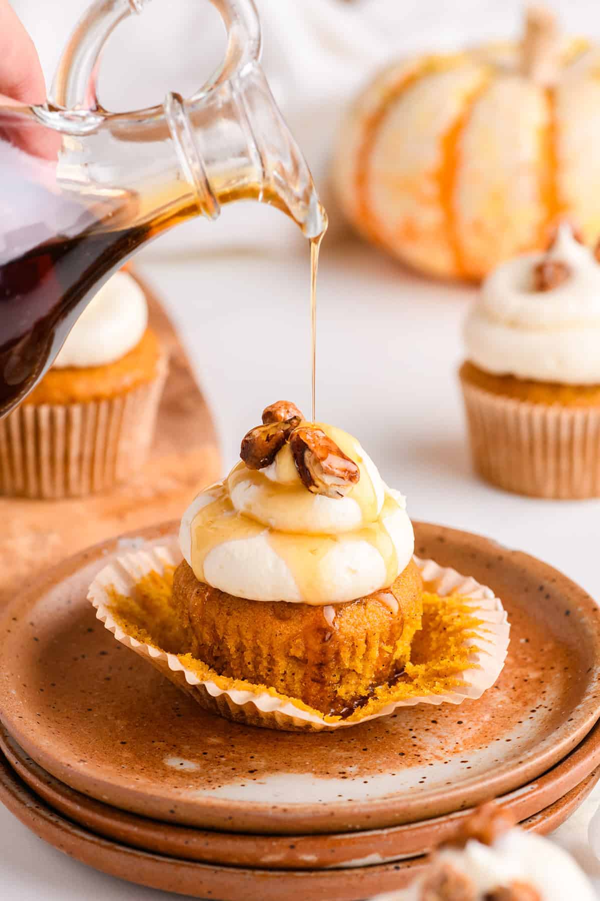 Shot of one Pumpkin Cupcake with Maple Cream Cheese Frosting getting maple syrup poured on top.