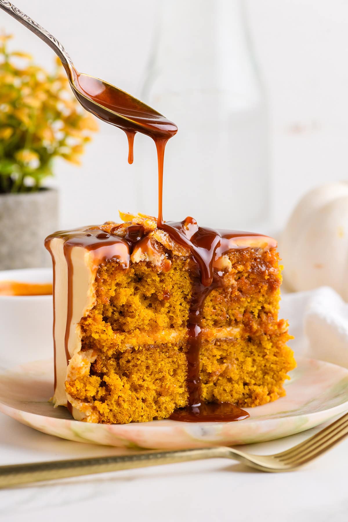 Close up of sliced Pumpkin Spice Layer Cake with Caramel Cream Cheese Frosting with caramel sauce being drizzled on top.