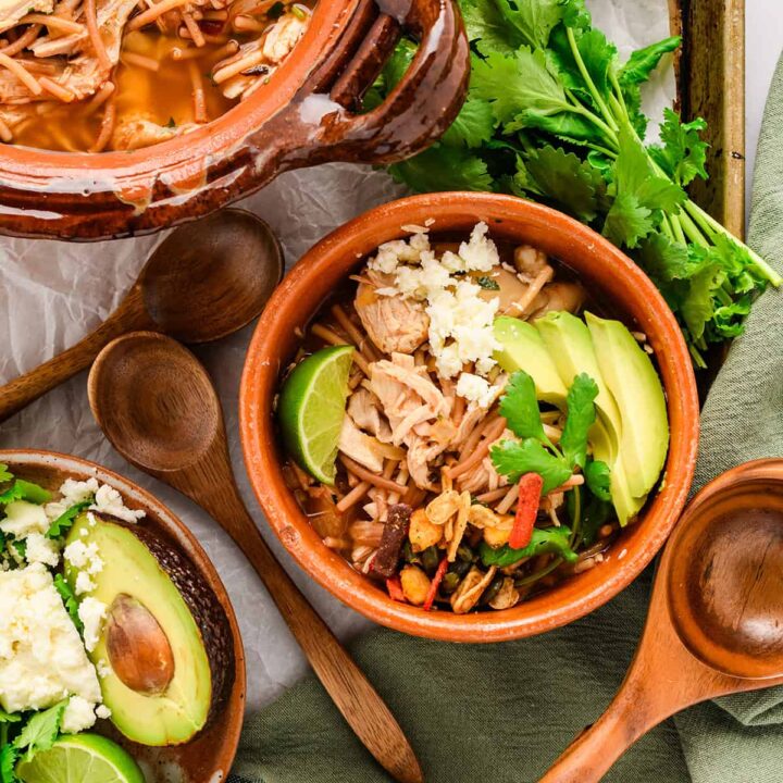 Overhead shot of Chicken Fideo Soup on baking sheet with serving pot and garnishes.