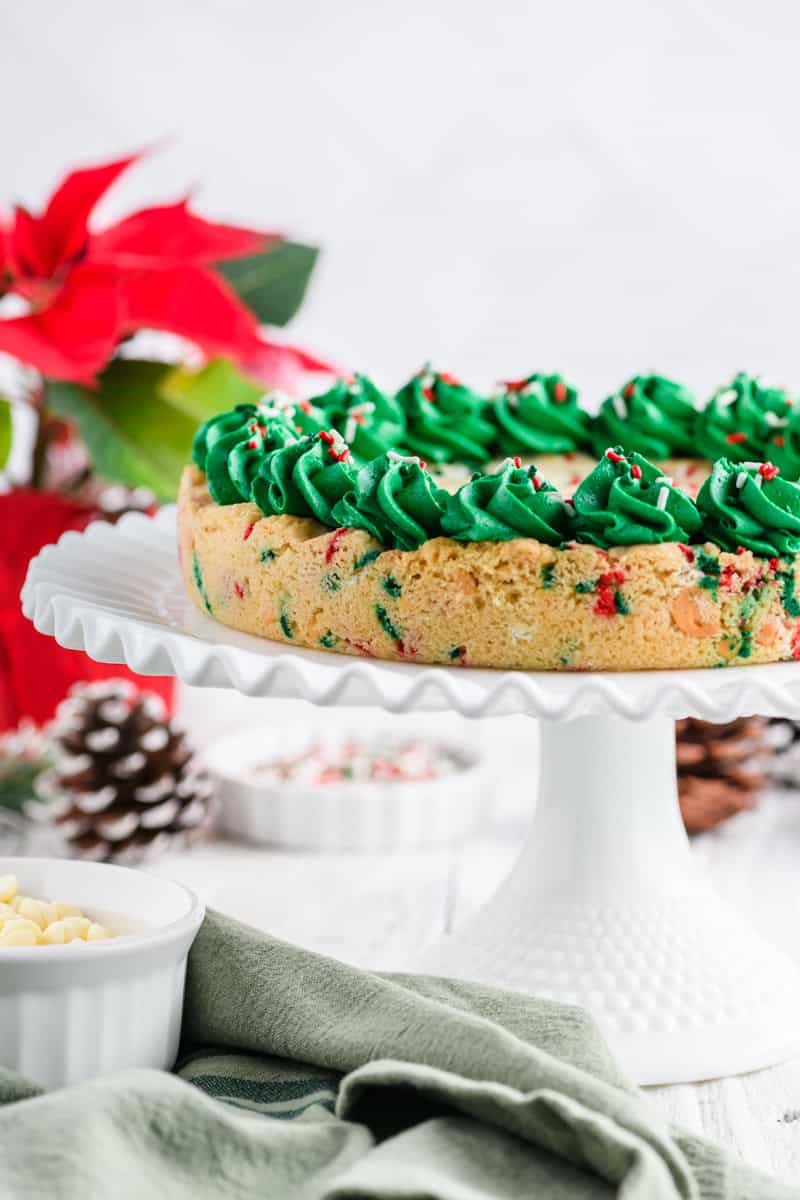 Head on angle of the side of the Christmas Confetti Cookie Cake on white cake pedestal.