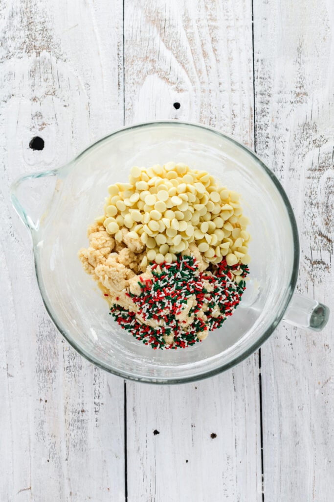 Overhead shot of sprinkles and white chocolate chips in cookie dough for Christmas Confetti Cookie Cake.