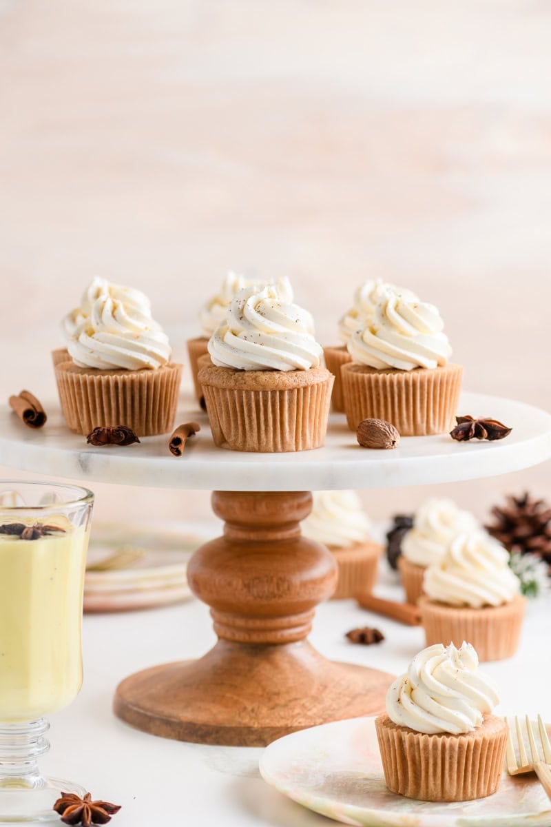 Pulled back shot of Eggnog Cupcakes on marble cake pedestal.