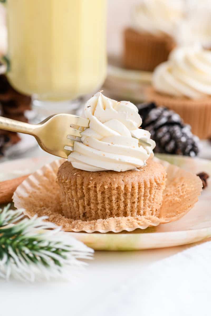 Close up a one Eggnog Cupcake on a plate with a fork slicing through it.