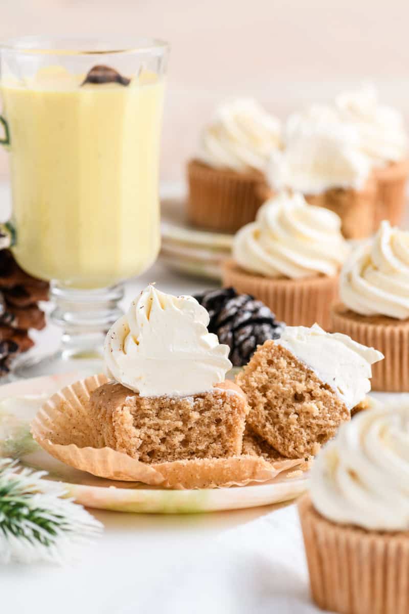 Wide open shot of a sliced Eggnog Cupcake with more Eggnog Cupcakes in the background. 