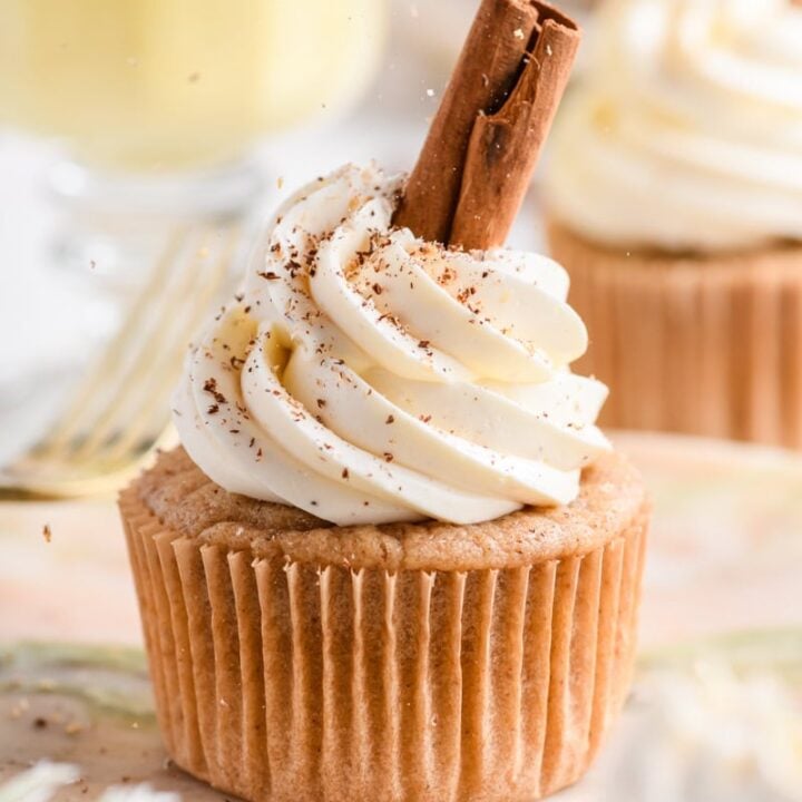 Close up of single Eggnog Cupcakes on a plate garnished with a cinnamon stick and sprinkling of nutmeg.