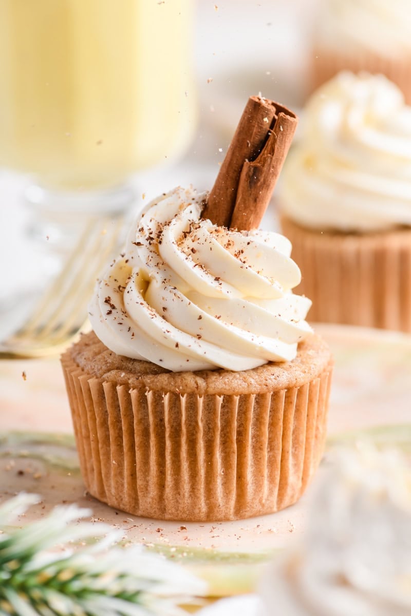 Close up of single Eggnog Cupcakes on a plate garnished with a cinnamon stick and sprinkling of nutmeg.