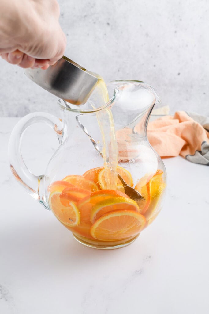 Process shot of orange juice being poured into the pitcher for Simple Sangria.