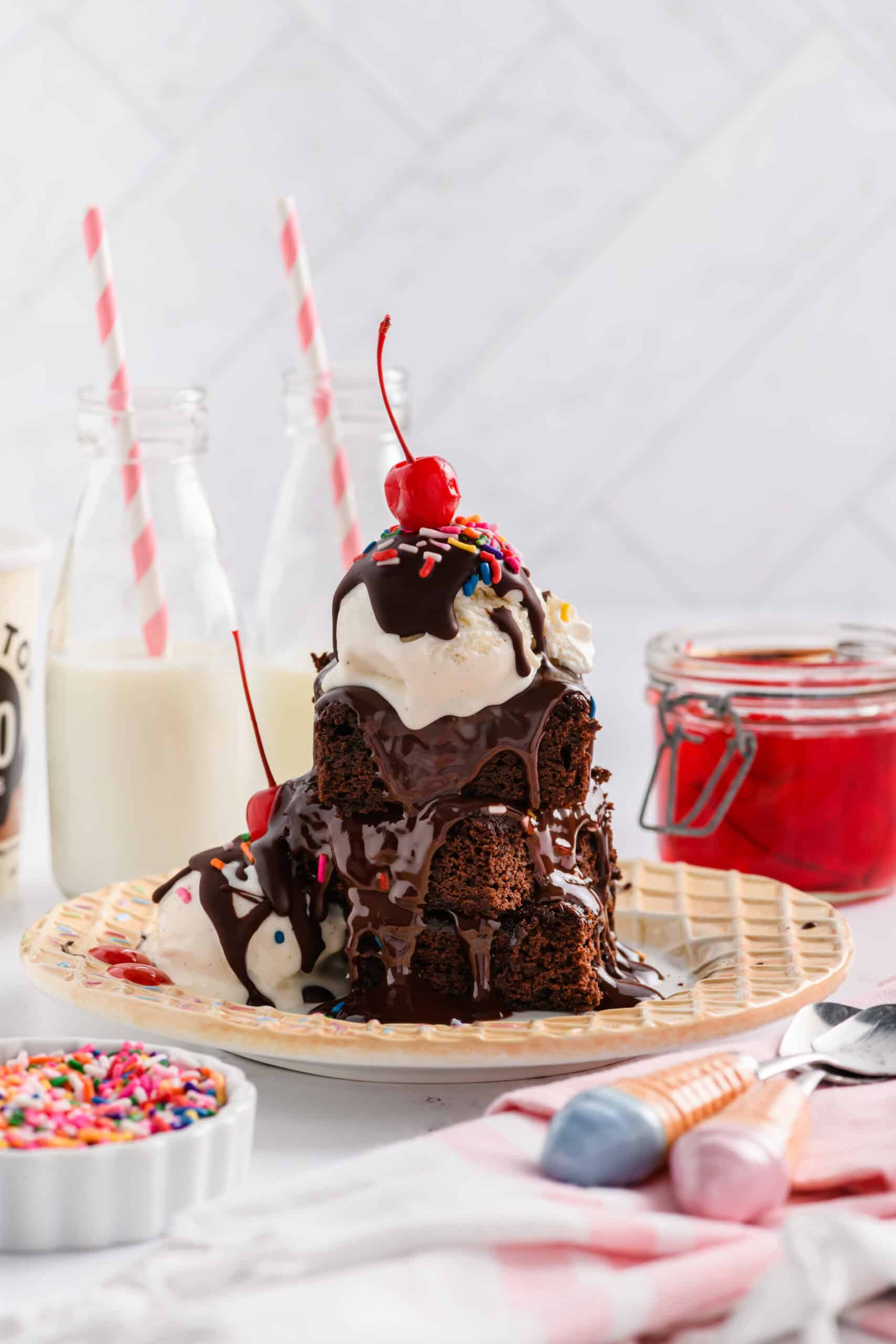 Wide open shot of Lightened Up Brownie a la Mode stacked 3 brownies high with chocolate sauce, sprinkles and maraschino cherry.