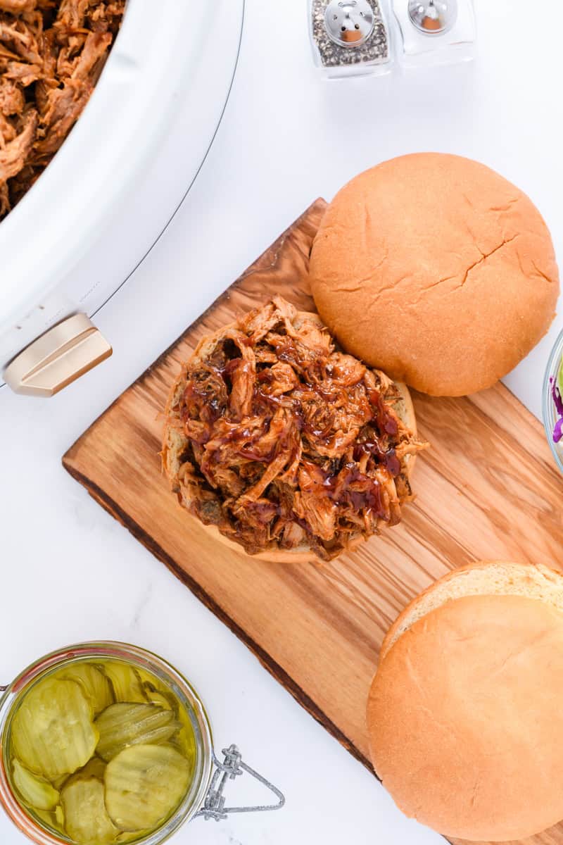 Overhead shot of pulled pork on open faced bun with slow cooker in the corner.
