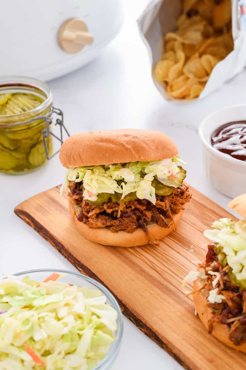 Angled shot of Slow Cooker Pulled Pork Sandwiches on wood serving board.