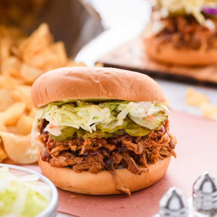 Close up shot of Slow Cooker Pulled Pork Sandwich with chips and second sandwich in the background.