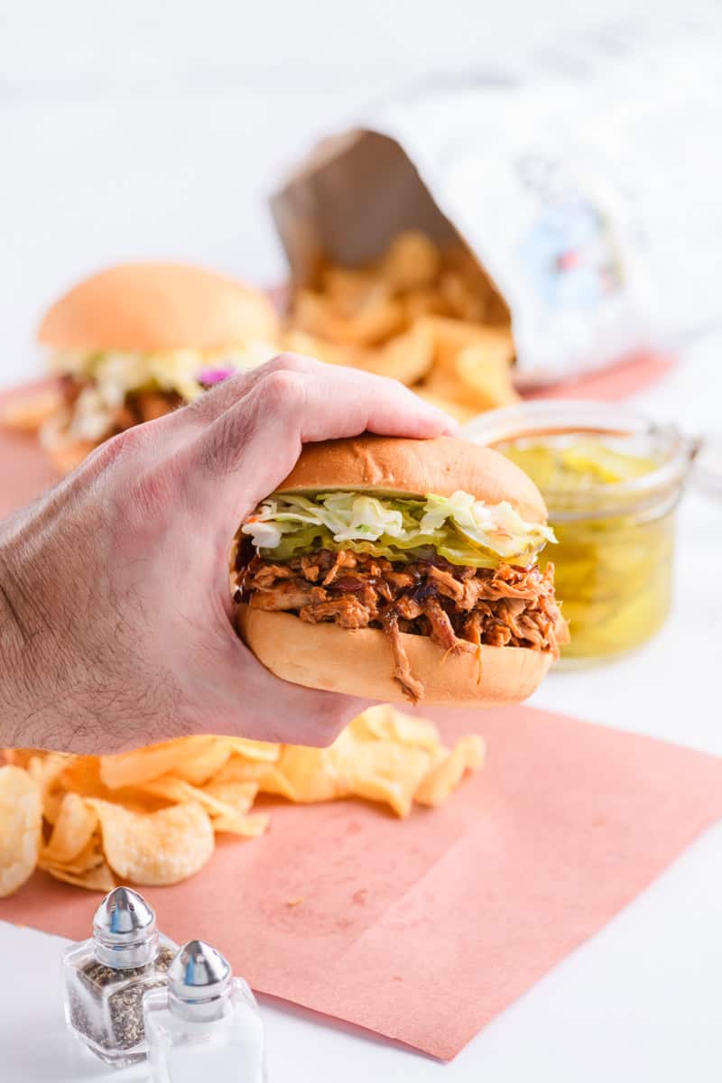 Man hands holding Slow Cooker Pulled Pork Sandwich.