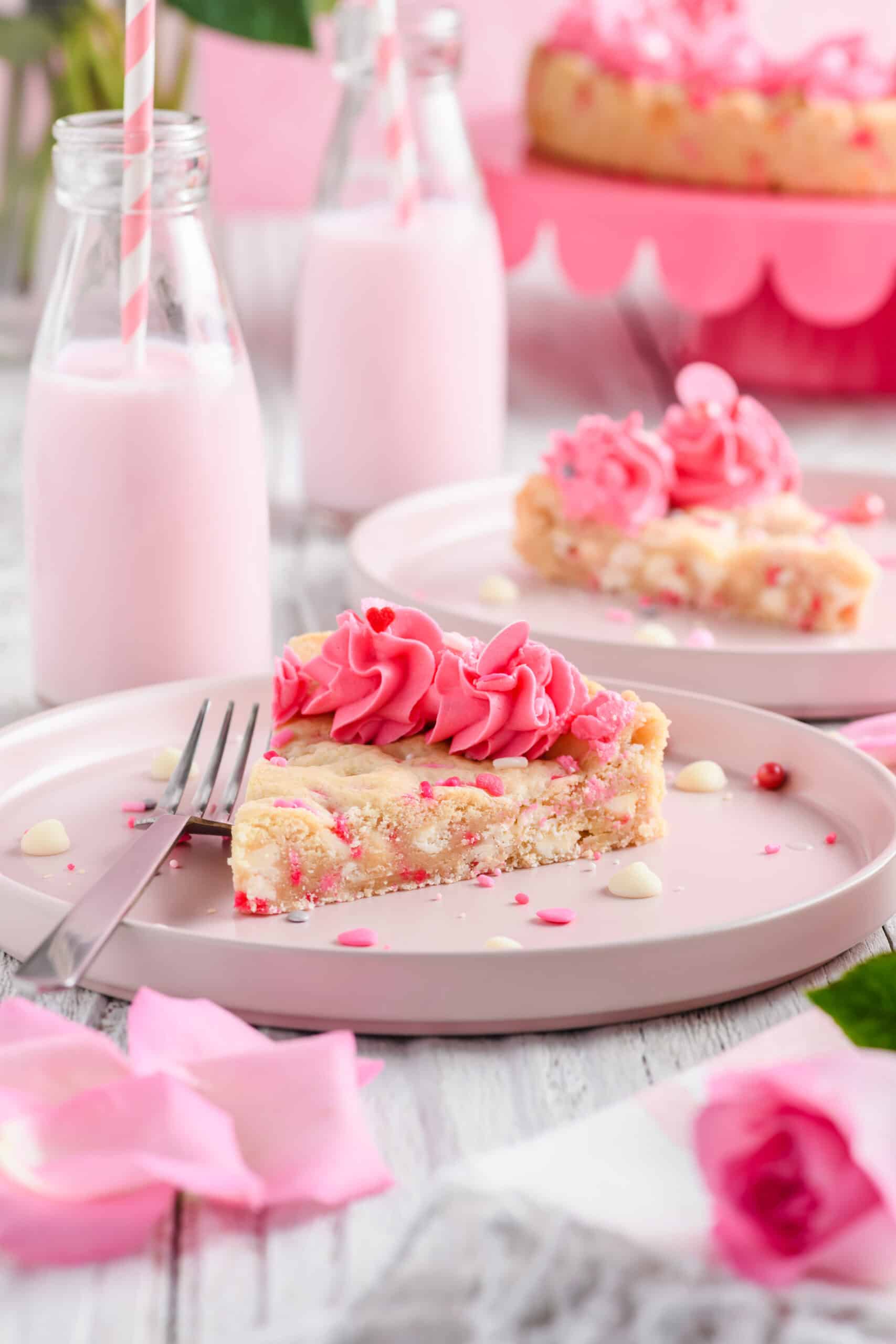 Shot of sliced Valentine Confetti Cookie Cake on pink plate with strawberry milk in the background.