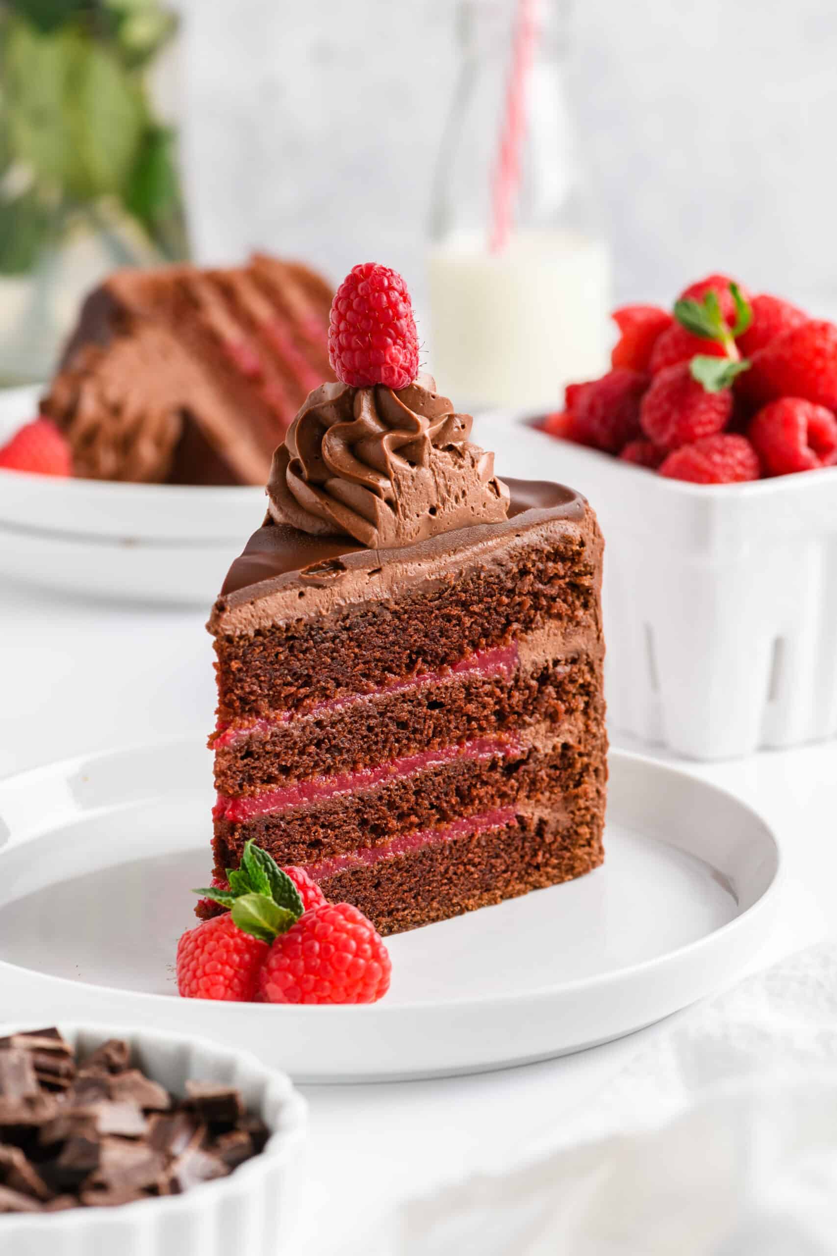 Close up of slice of Chocolate Raspberry Cake with Whipped Cream Ganache Frosting on white plate.