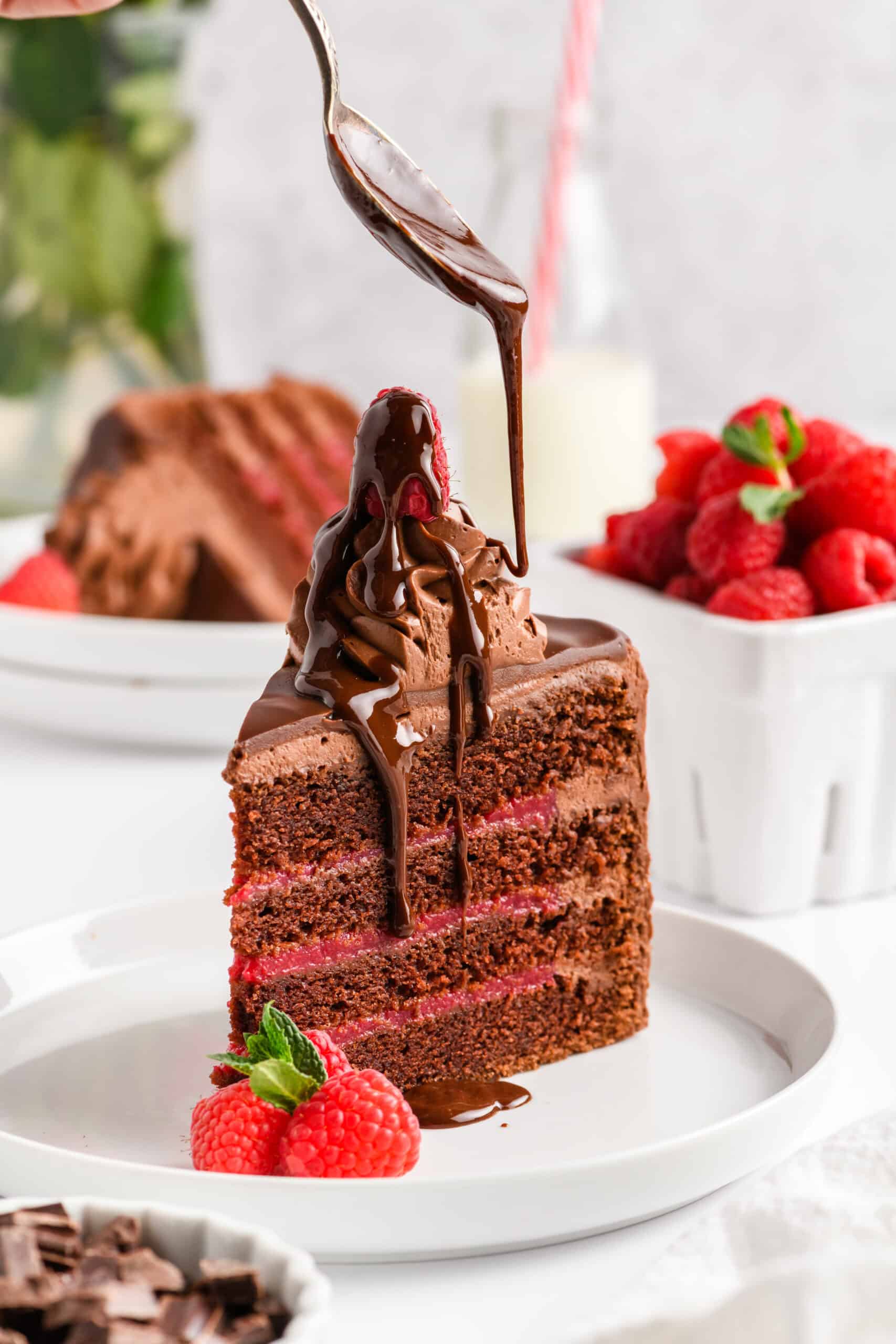 Close up shot of a slice of Chocolate Raspberry Cake with Whipped Ganache with chocolate drip being drizzled on top.