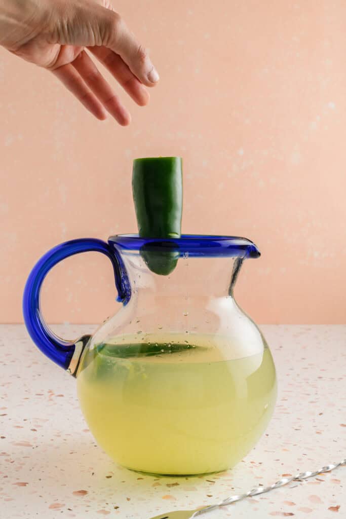 Process shot of fresh jalapeño going into Jalapeño Margaritas pitcher.