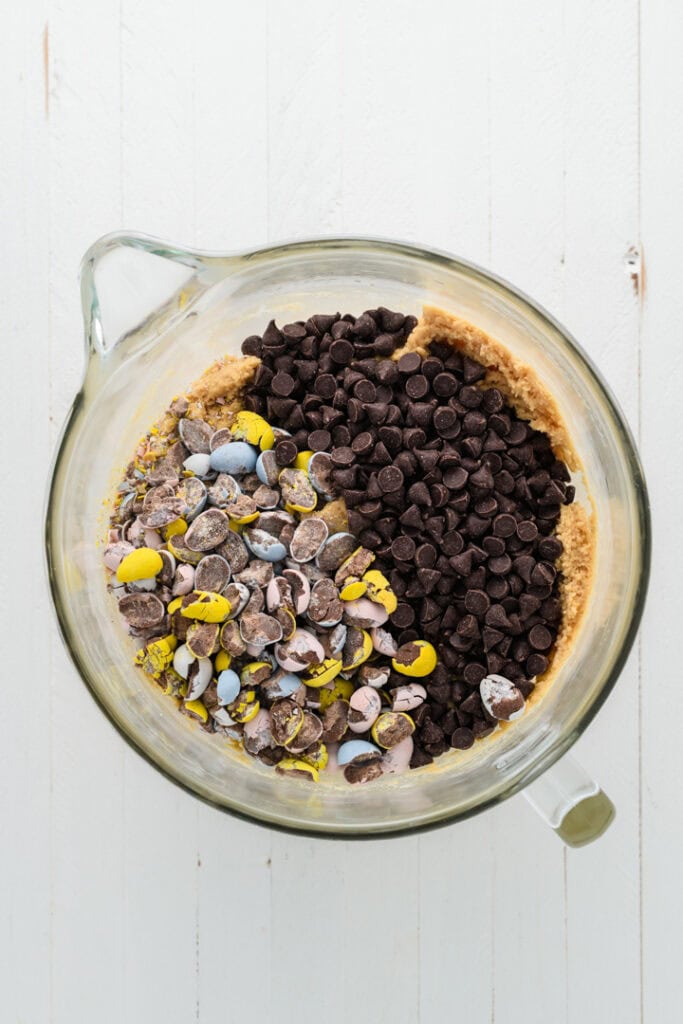 Overhead shot of chocolate chips and chocolate Easter candy on cookie dough for Easy Easter Chocolate Chip Cookies.