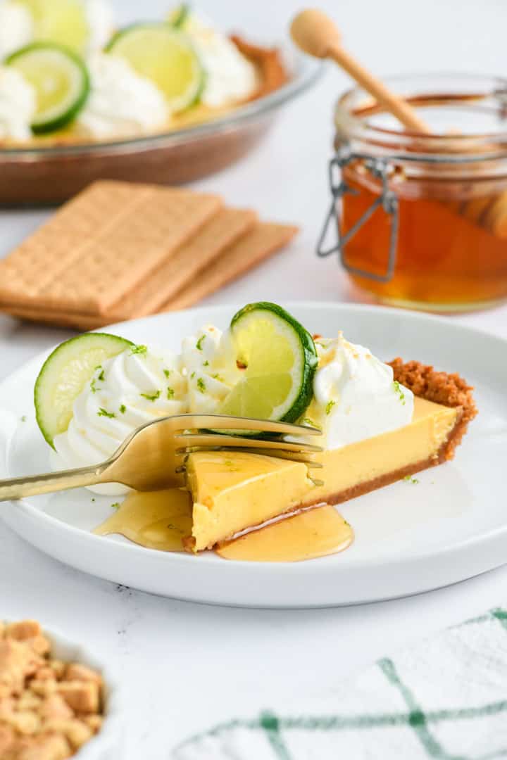 Key Lime Pie slice on plate with honey with a fork cutting through it.