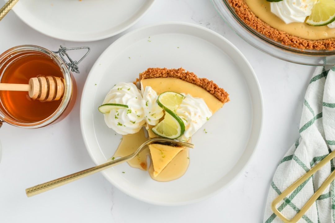 Landscape overhead shot of sliced Key Lime Pie on plate with honey and fork cutting through it.