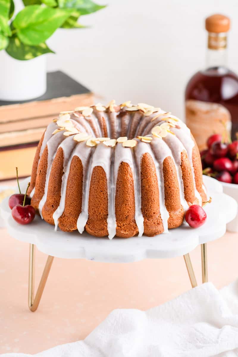 Whole Amaretto Bundt Cake on marble cake stand at slight angle.