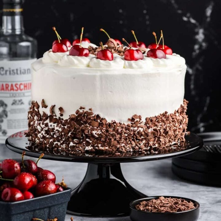Black Forest Cake on black cake stand with crate of cherries and cherry liqueur.
