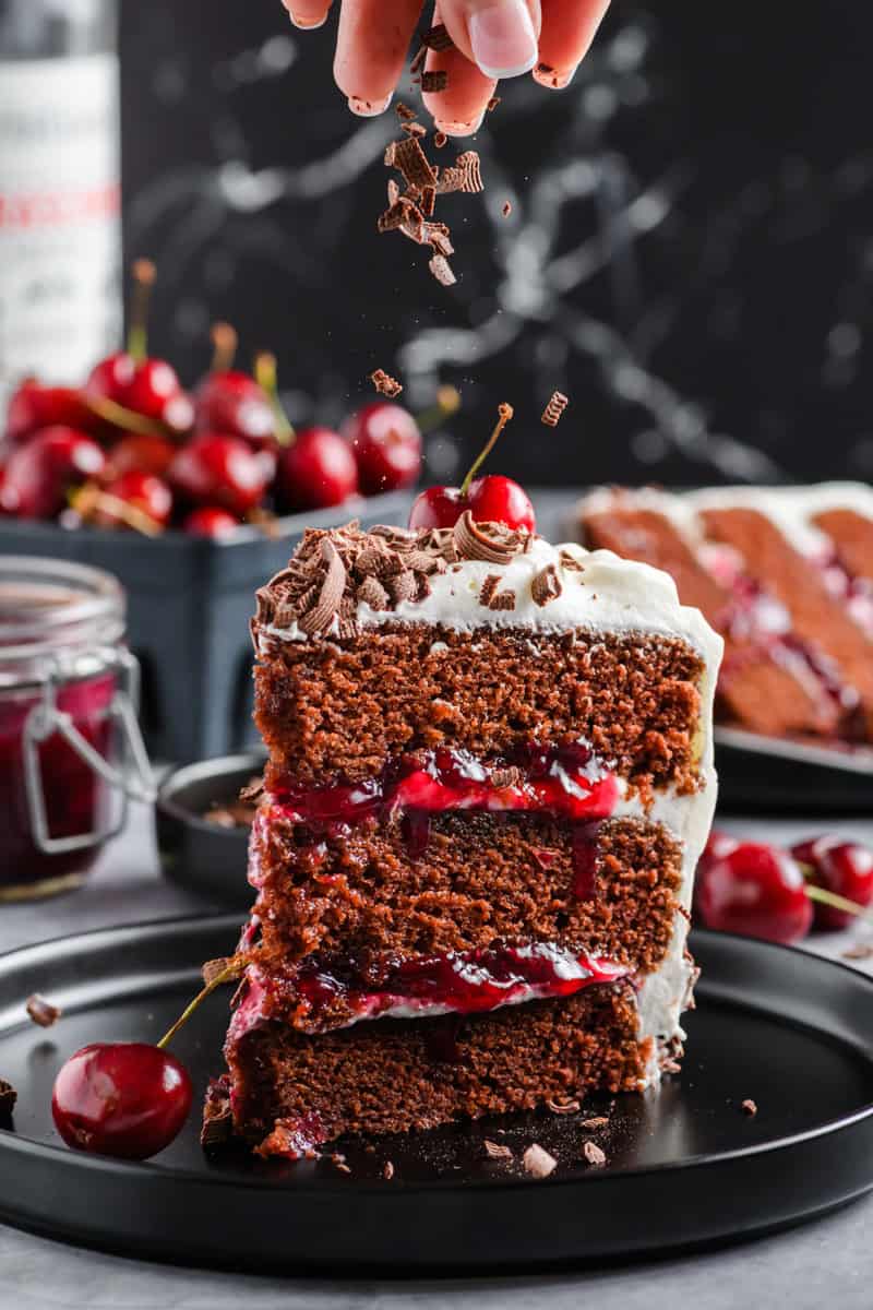 Slice of Black Forest Cake with chocolate curls being sprinkled on top.
